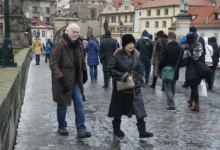 Crowded cobblestone street in a historic town with people wearing winter coats and fur, foreground man and woman looking toward the camera.