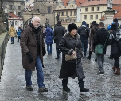 Crowded cobblestone street in a historic town with people wearing winter coats and fur, foreground man and woman looking toward the camera.