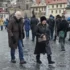 Crowded cobblestone street in a historic town with people wearing winter coats and fur, foreground man and woman looking toward the camera.