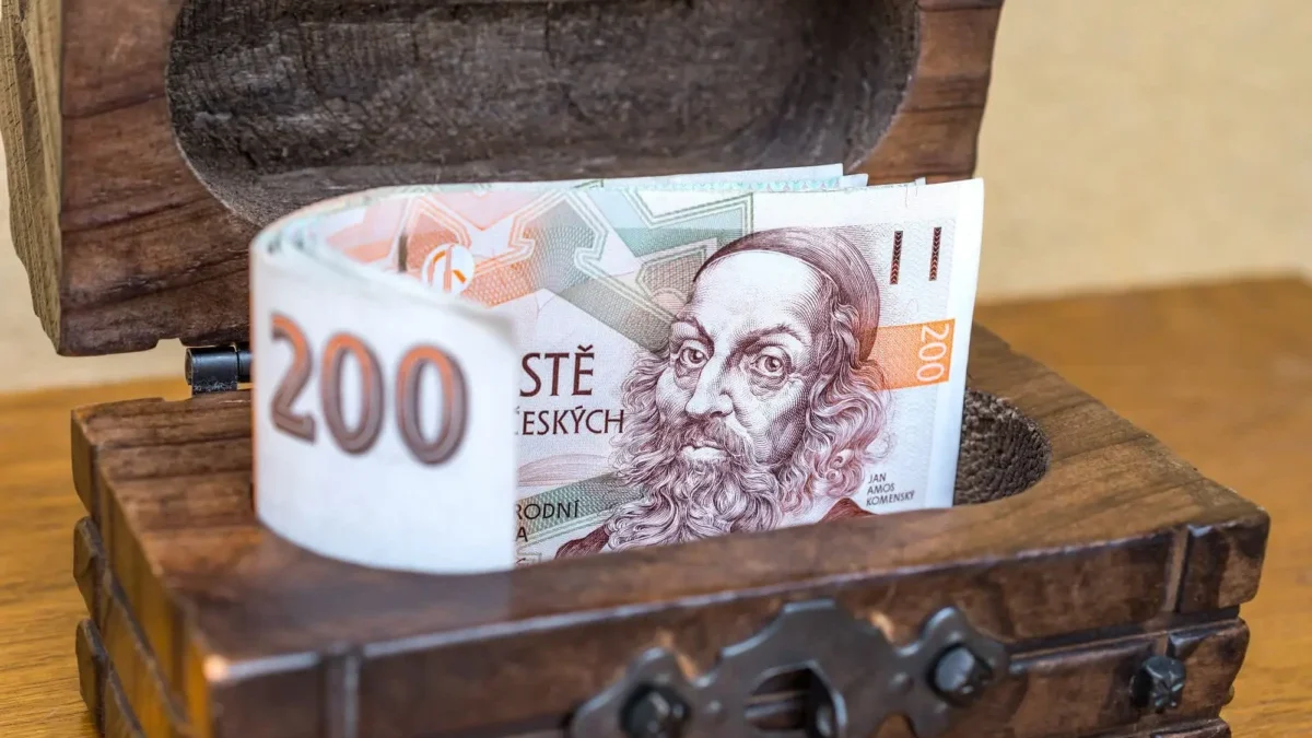 české bankovky vykukující z dřevěné truhličky
