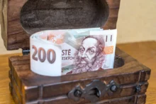 české bankovky vykukující z dřevěné truhličky