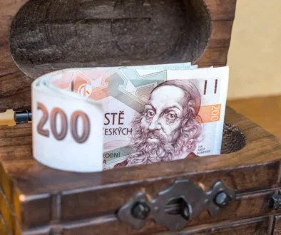 české bankovky vykukující z dřevěné truhličky