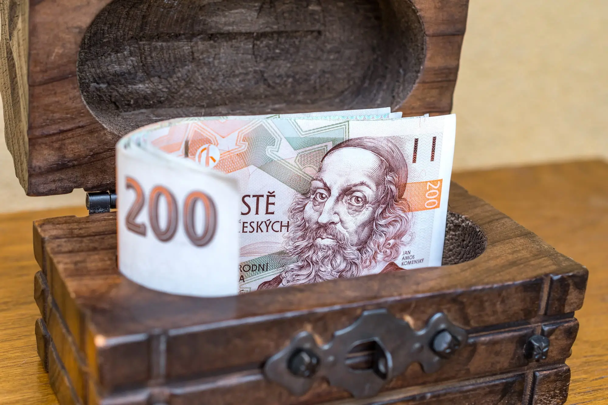 české bankovky vykukující z dřevěné truhličky