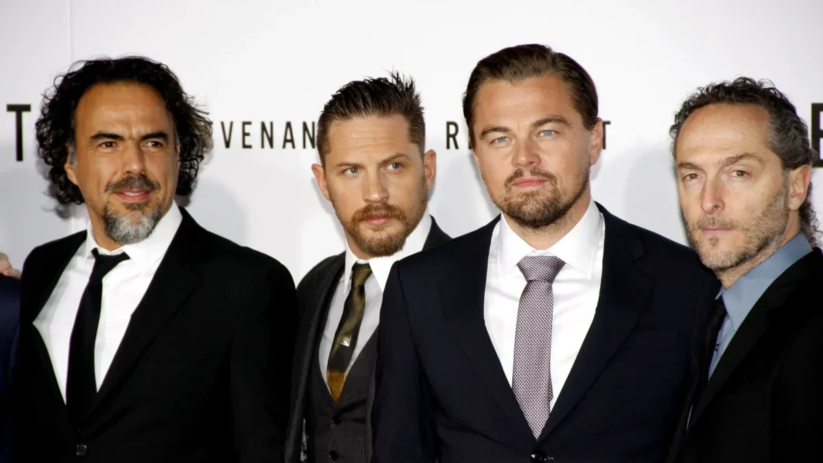 Four men in black suits posing together at a formal event/photo backdrop on a red carpet area.