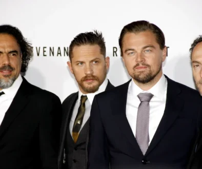 Four men in black suits posing together at a formal event/photo backdrop on a red carpet area.