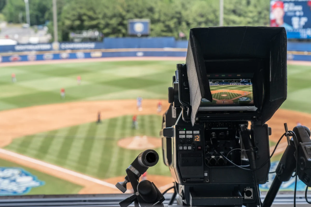 shutterstock_1407332594 1 | TVGURU.cz Broadcast camera on a tripod overlooking a baseball field, showing the in-camera monitor displaying the field while recording a game.