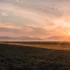 Sunset over a flat farmland with distant mountains and a warm orange glow across the sky and ground.—landscape.