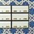 Row of white metal mailboxes with brass slots and locks, mounted on a black frame against a blue-and-white tiled wall.