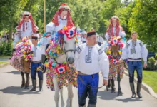 Group of people in traditional embroidered costumes riding horses decorated with rainbow paper garlands in a festive parade outdoors.