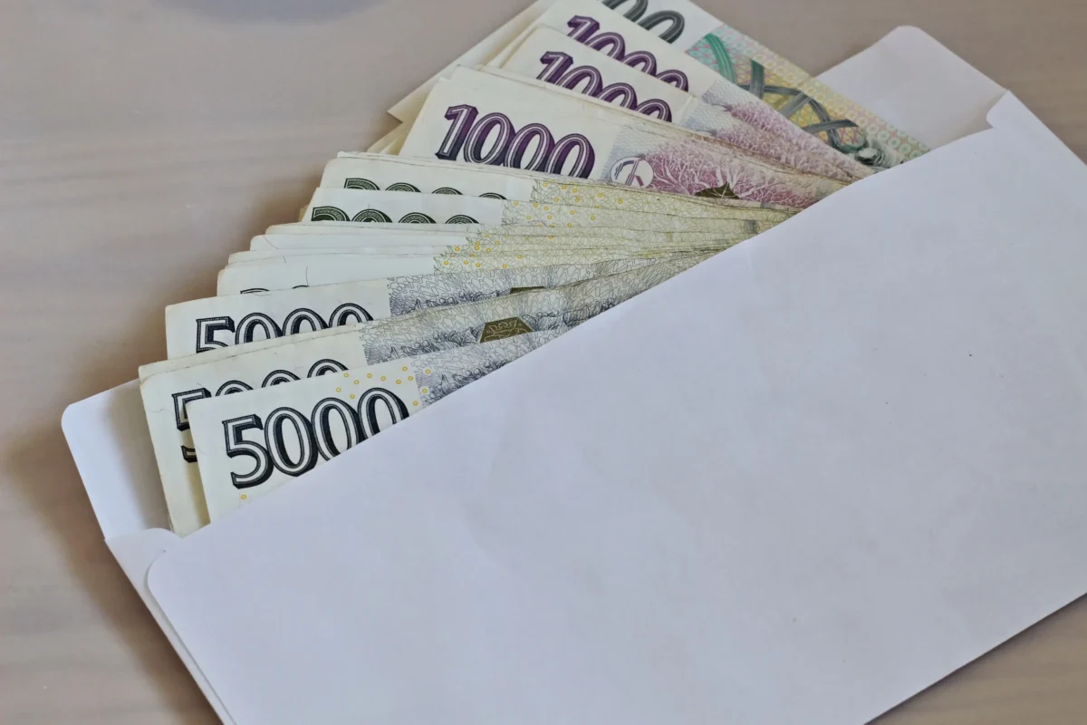 Z obálky vyčuhují české bankovky.