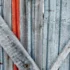 Weathered vertical wooden slats with peeling gray paint, crossed by a diagonal weathered board and a narrow red strip visible behind.