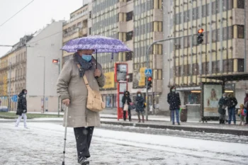 Žena s rouškou a deštníkem jde po chodníku.