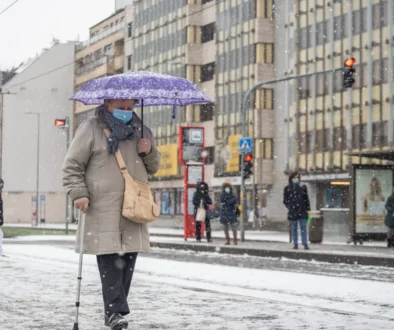 Žena s rouškou a deštníkem jde po chodníku.