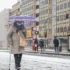Žena s rouškou a deštníkem jde po chodníku.