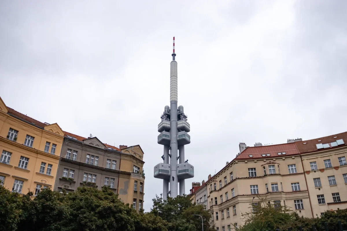 Tall communications tower rises above surrounding city buildings under a cloudy sky, centered in the frame.