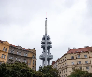 Tall communications tower rises above surrounding city buildings under a cloudy sky, centered in the frame.