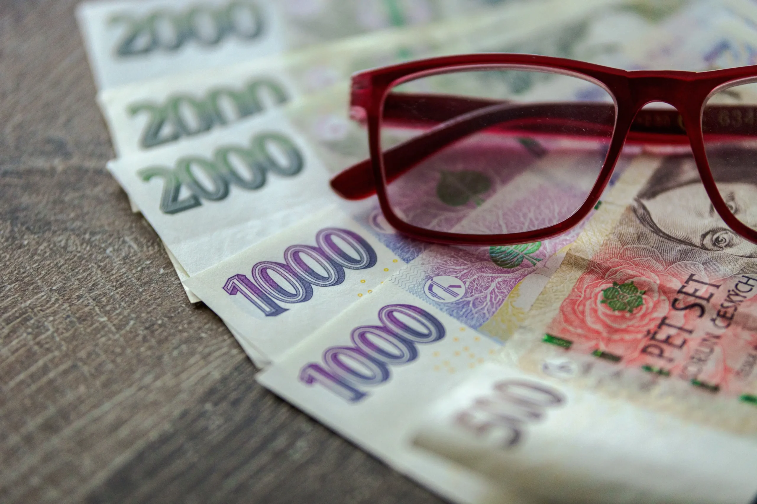 shutterstock_2500104855-2-2 | TVGURU.cz České bankovky vyskládané na stole a na nich položené brýle.