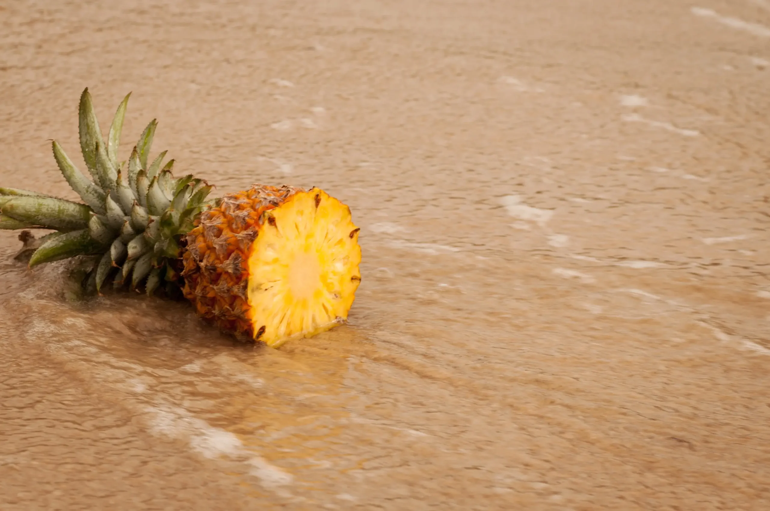 Pineapple half with green crown resting on a wooden table surface.