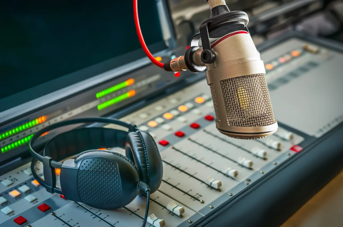 shutterstock_2467610471 1 | TVGURU.cz Professional studio microphone mounted over a sound mixing console with headphones resting nearby in a radio/recording studio.