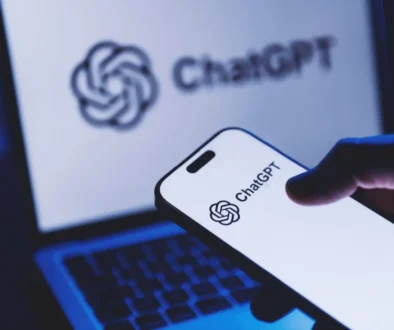 Close-up of a smartphone displaying the ChatGPT logo, with a laptop screen showing ChatGPT in the blurred background.