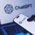 Close-up of a smartphone displaying the ChatGPT logo, with a laptop screen showing ChatGPT in the blurred background.