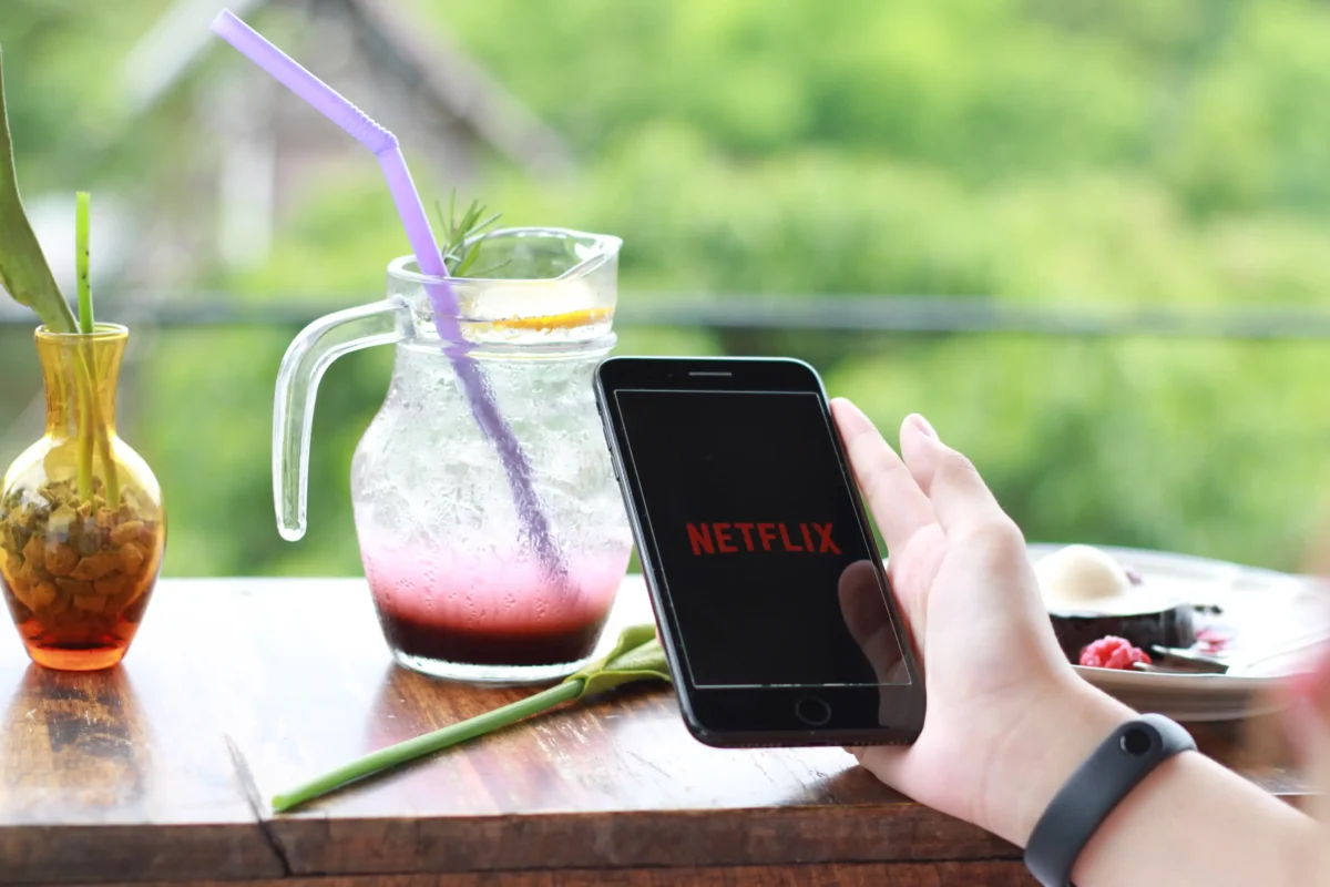 shutterstock_1789338983-2 | TVGURU.cz Člověk v ruce drží mobil s Netflixem a na stole za ním stojí džbánek.