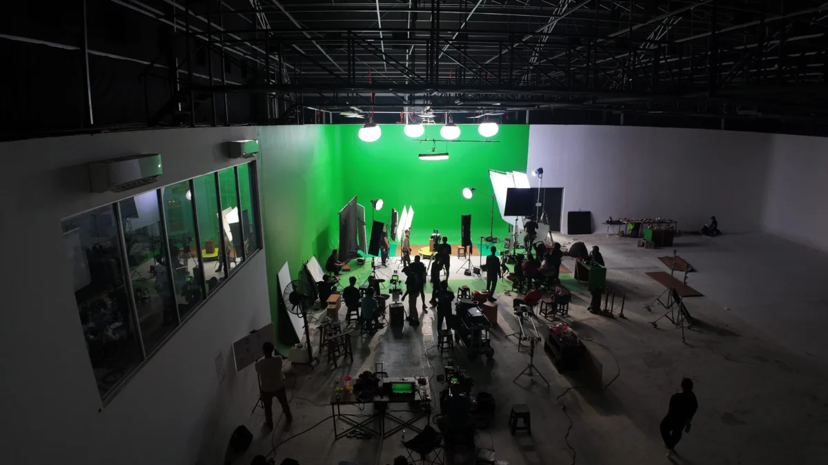 shutterstock_2673710951 1 | TVGURU.cz Behind-the-scenes view of a video studio with a bright green chroma key wall, multiple lights, cameras, and crew preparing for filming.