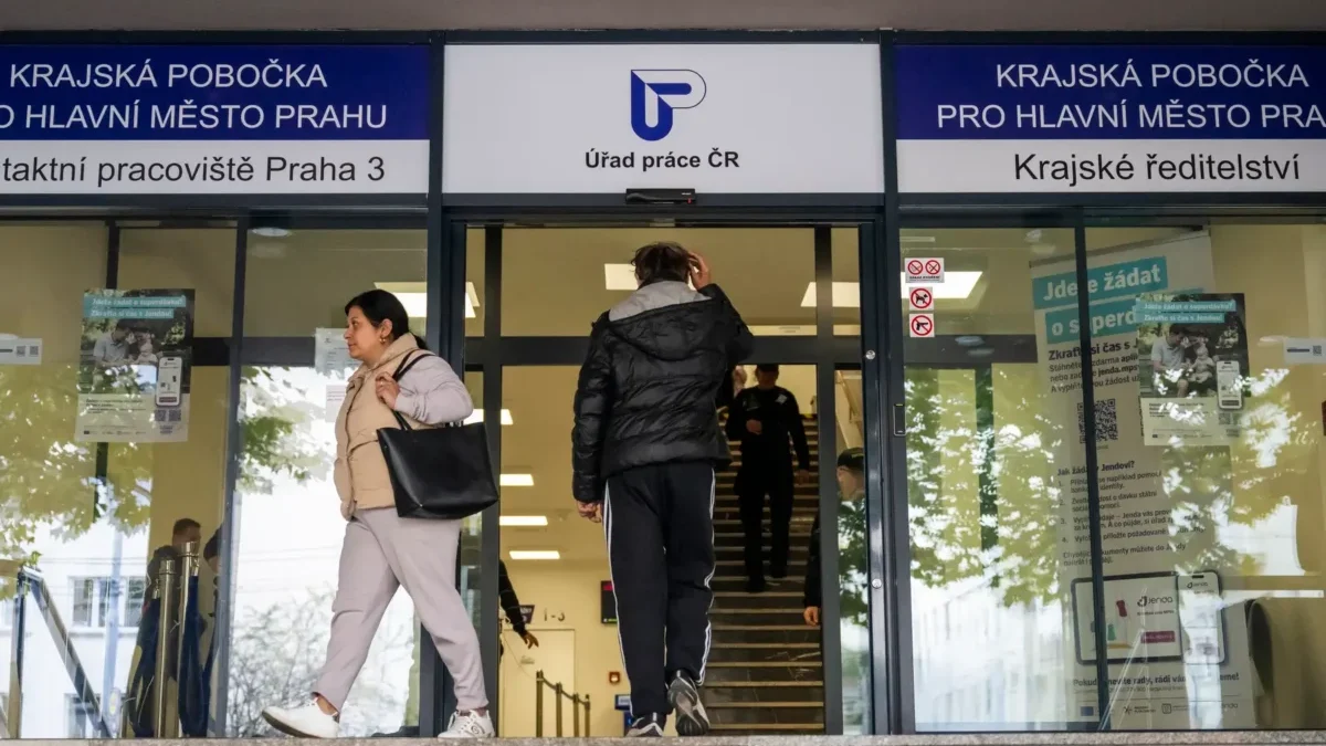 Two people exit a Czech public service office under blue signage that says Úřad práce ČR above glass doors.