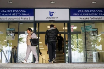 Two people exit a Czech public service office under blue signage that says Úřad práce ČR above glass doors.