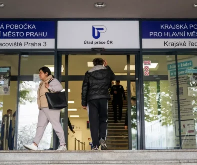 Two people exit a Czech public service office under blue signage that says Úřad práce ČR above glass doors.