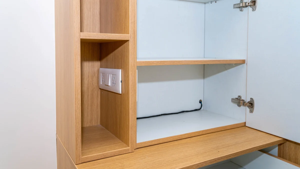 shutterstock_1947231022 1 | TVGURU.cz Open wooden cabinet with shelves, showing a wall outlet on the left inner panel and a black cable along the back edge.