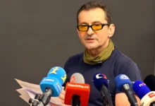muž v brýlích s mikrofony před sebou