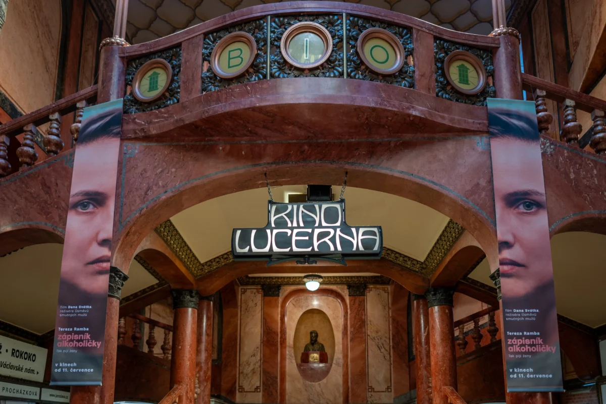 shutterstock_2785110611 1 | TVGURU.cz Interior of a marble theater or cinema lobby with a curved balcony, banners featuring a woman's face on either side, and a central sign that reads 'KINO'.