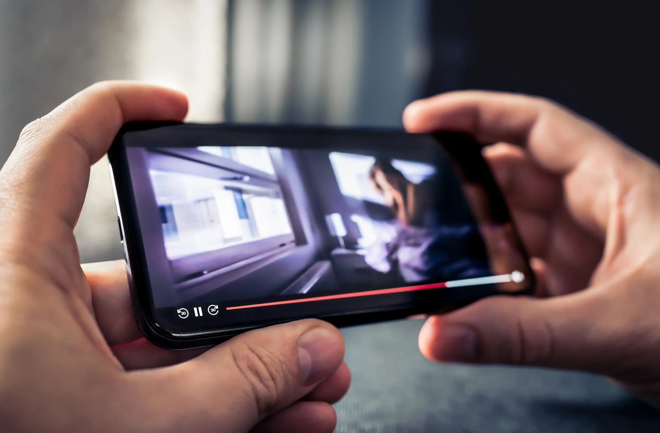 shutterstock_2274357759 | TVGURU.cz Ruce drží mobilní telefon, ne kterém je puštěné video.