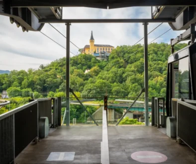 View from a tram platform toward a yellow hilltop building surrounded by green trees, with metal framework and rails in the foreground.