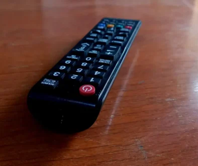 Black TV remote lying on a wooden table, angled to the left with a red power button visible at the bottom corner.