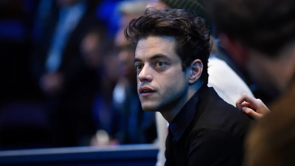 Close-up of a young man with dark hair in a black shirt, looking to the left in a dimly lit crowd.
