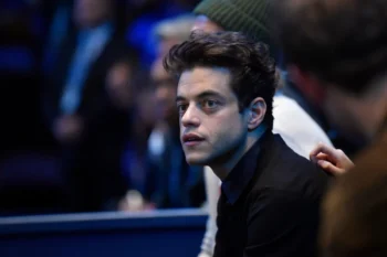 Close-up of a young man with dark hair in a black shirt, looking to the left in a dimly lit crowd.
