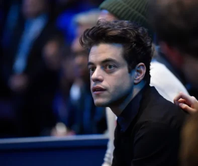 Close-up of a young man with dark hair in a black shirt, looking to the left in a dimly lit crowd.