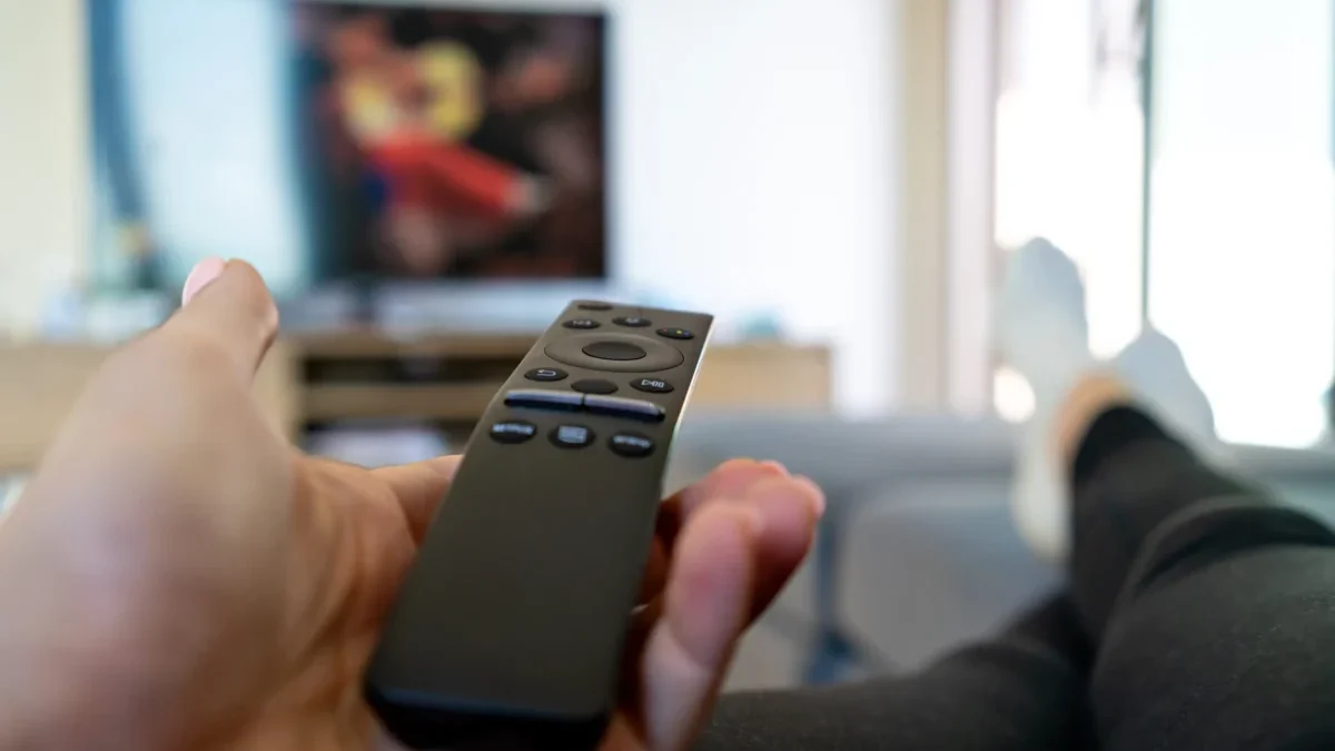 Člověk leží a míří ovladačem na TV