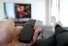 Člověk leží a míří ovladačem na TV