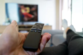 Člověk leží a míří ovladačem na TV