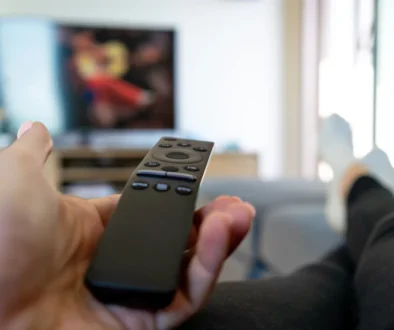 Člověk leží a míří ovladačem na TV