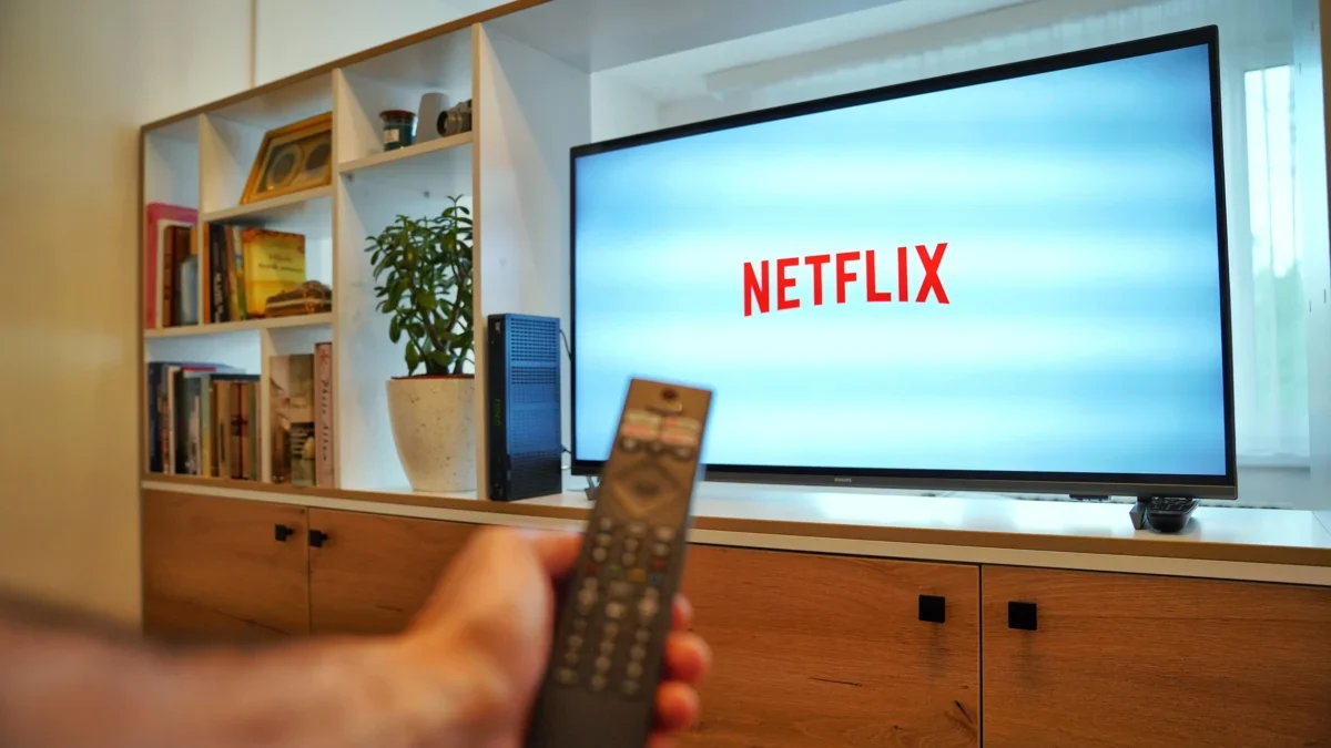 Person holding a remote in front of a TV displaying the Netflix logo in a living room setting