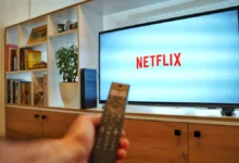 Person holding a remote in front of a TV displaying the Netflix logo in a living room setting