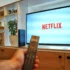 Person holding a remote in front of a TV displaying the Netflix logo in a living room setting