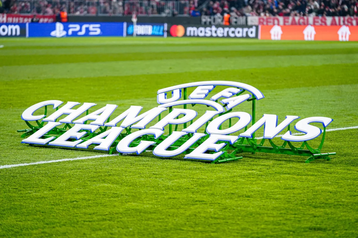shutterstock_2729394743 1 | TVGURU.cz 3D Champions League sign on a soccer pitch with green grass and a blurred stadium crowd in the background