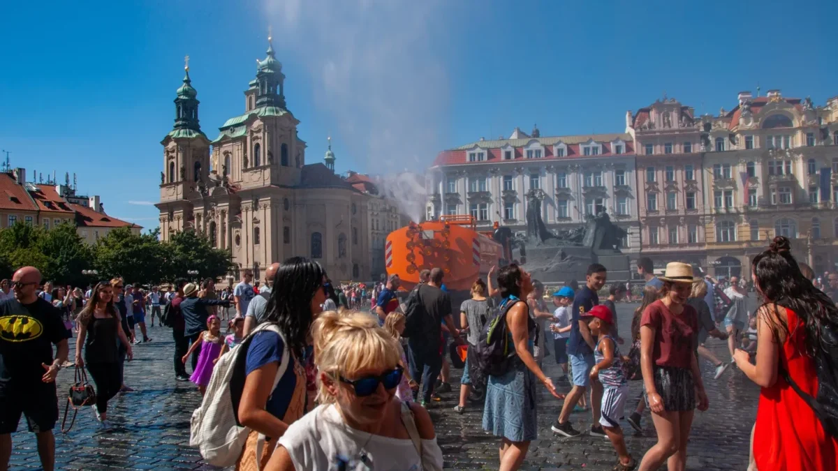 Lidé jsou v Praze na náměstí a kolem stříká voda.