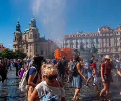 Lidé jsou v Praze na náměstí a kolem stříká voda.