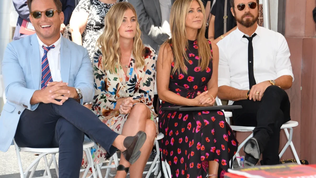 Jennifer Aniston sedí mezi lidmi.